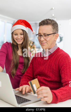 Lächelnd, Vater und Tochter während der Weihnachtszeit zu Hause online-shopping Stockfoto