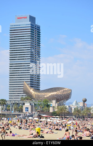 Sonnenanbeter am Strand von Barceloneta mit Gehrys Fisch, Peix, Skulptur und Mapfre Tower-Gebäude. Barcelona, Katalonien, Spanien. Stockfoto