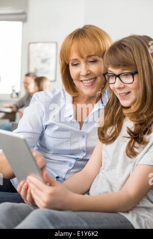 Glückliche Mutter und Tochter mit tablet-PC mit Familie sitzt im Hintergrund zu Hause Stockfoto