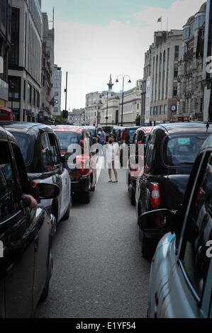 Eine Frau steht in der Mitte der Straße und nimmt ein Foto auf Ihrem Handy der Taxi the Strand blockieren in London, England während ein Taxifahrer Protest über das Handy app Uber. Stockfoto