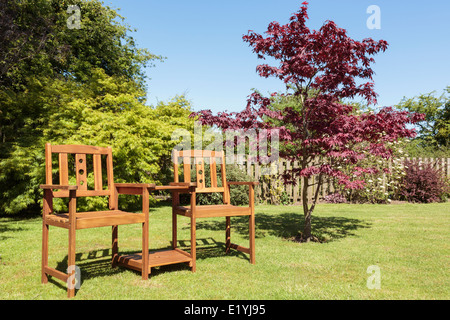 Holz-Beifahrersitz oder Liebestuhlbank mit Tisch zwischen zwei Sitzen von einem Acer Baum auf einem Haushalt Garten Garten Garten Garten Garten im Sommer. Großbritannien Stockfoto