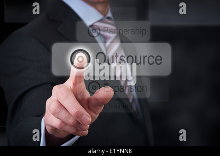 Ein Geschäftsmann deuten auf eine Business-Outsourcing-Taste auf einen klaren Bildschirm. Stockfoto