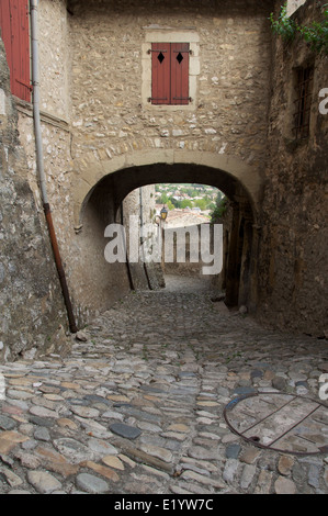 Eine schmale gepflasterte Gasse, Rue St François, führt nach unten aus dem Tour-de-Kamm in die Altstadt, Unterquerung einer mittelalterlichen Torbogen. La Drôme, Frankreich. Stockfoto