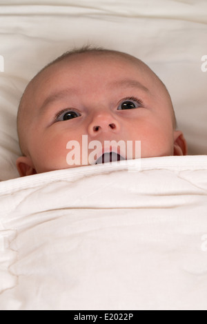 Baby ist überrascht mit Mund offen im Bett liegend Stockfoto