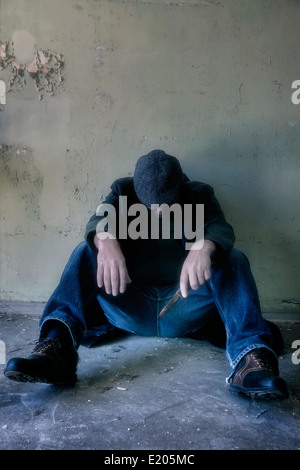 ein Mann mit einem Messer sitzen auf dem Boden in einem verlassenen Haus Stockfoto