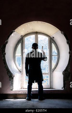 ein Mann mit einem Gewehr vor einem alten Fenster in einem verlassenen Gebäude Stockfoto