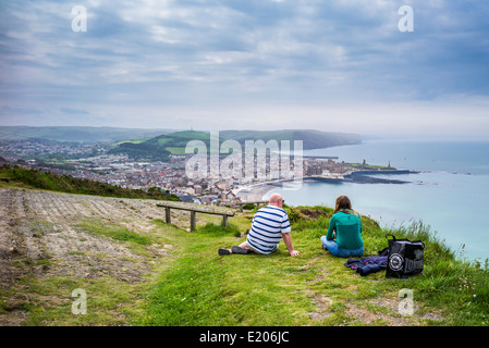 Älteres Paar, Mann und Frau sitzen auf dem Rasen an der Spitze der Verfassung Hill Aberystwyth Blick auf Cardigan Bay Stockfoto
