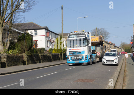 Groß, breit-laden, Erdbewegungsmaschinen Muldenkipper auf einen Volvo FH16 Tieflader durch ein Dorf im Nordwesten Englands transportiert werden. Stockfoto