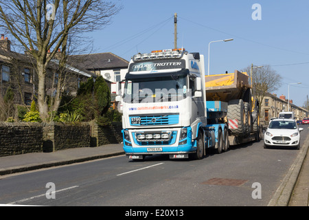 Groß, breit-laden, Erdbewegungsmaschinen Muldenkipper auf einen Volvo FH16 Tieflader durch ein Dorf im Nordwesten Englands transportiert werden. Stockfoto