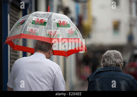 Ein Mann mit einem Regenschirm mit walisischen Fahnen geschmückt geht auf einer Straße im Regen. Stockfoto