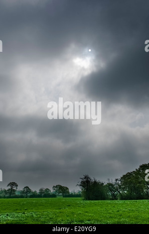 Sonne durch dicke graue Wolken über englische Landschaft; im Hochformat. Stockfoto