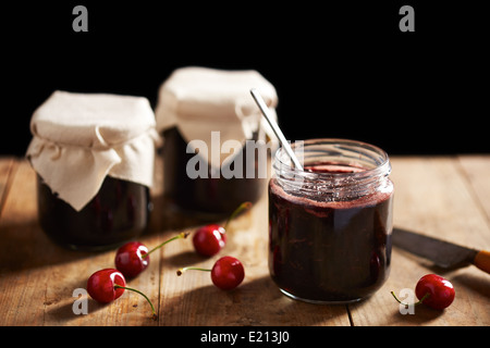 Selbstgemachte Kirschmarmelade in Gläsern auf Holztisch Stockfoto