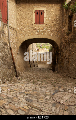 Eine schmale gepflasterte Gasse, Rue St François, führt nach unten aus dem Tour-de-Kamm in die Altstadt, Unterquerung einer mittelalterlichen Torbogen. La Drôme, Frankreich. Stockfoto