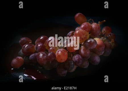 Rote Trauben in Rotwein auf schwarzem Hintergrund Stockfoto