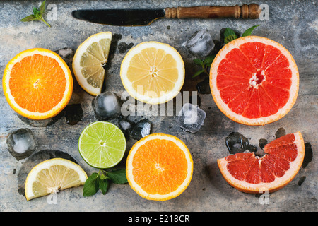 Satz von geschnittenen Zitrusfrüchten Zitrone, Limette, Orange, Grapefruit mit Minze, Eis und Vintage Messer über Metall Hintergrund. Ansicht von oben. Stockfoto