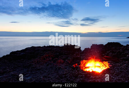 kleines Lagerfeuer auf felsigen Küste in der Nacht Stockfoto