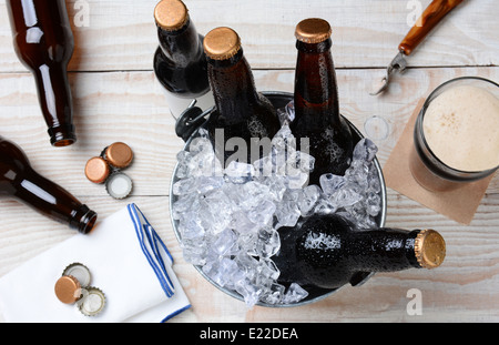 Hohen Winkel Schuss von einem Glas Bier mit einem Blecheimer mit ungeöffneten Flaschen. Die rustikalen Holztisch hat leere Flaschen Stockfoto