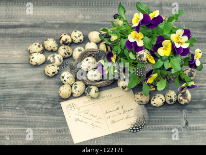 Oster-Deko mit Stiefmütterchen Blumen, Wachteleiern und Grußkarte. Vintage-Stil getönten Bild Stockfoto