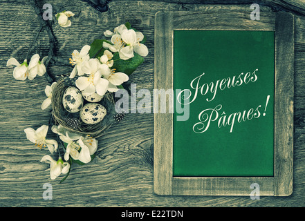 Tafel, Blumen und Ostern nest mit Eiern auf rustikalen hölzernen Hintergrund mit Beispieltext Frohe Ostern auf Französisch. Stockfoto
