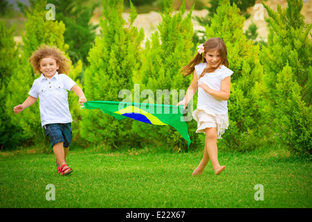 Glückliches Kind genießen Fußballmeisterschaft, Bruder und Schwester mit großer Brasilien-Flagge laufen, aktive und sportliche Kindheit Stockfoto