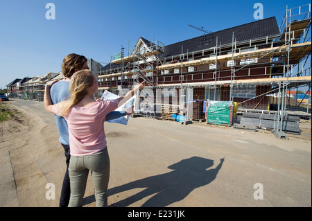 Junges Paar mit Blaupause sucht in neu gebauten Häusern auf Baumaschinen Stockfoto