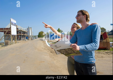 Junges Paar mit Blaupause sucht in neu gebauten Häusern auf Baumaschinen Stockfoto