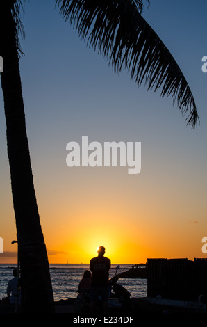 Silhouette einer Palme und Menschen den Sonnenuntergang am Strand von Waikiki auf der Insel Oahu in Hawaii. Stockfoto
