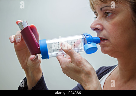 eine Frau mittleren Alters mit einem Asthma-Inhalator mit Abstandhalter um Symptome zu lindern Stockfoto