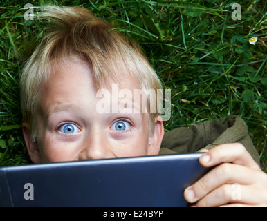 Porträt von Kind blonde junge spielt mit einem digital-Tablette pc Computer im Freien im park Stockfoto