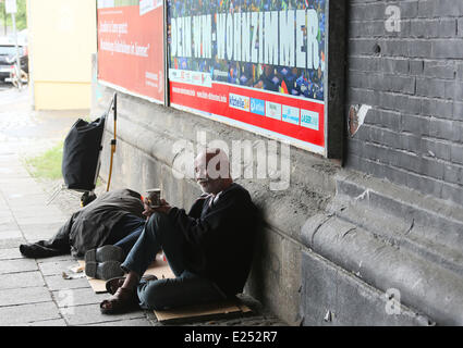 Berlin, Deutschland. 13. Juni 2014. Ein Obdachloser aus Bratislava sitzt vor einem Plakat lesen "Your World Cup-Wohnzimmer" unter einer Brücke am Bahnhof Friedrichstraße in Berlin, Deutschland, 13. Juni 2014. Der Slogan fördert das public Viewing im Alte Foersterei Stadium in Berlin. Foto: Stephanie Pilick/Dpa/Alamy Live News Stockfoto