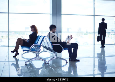 Zwei Geschäftspartner lesen am Flughafen im Hintergrund ihres Kollegen am Fenster stehend Stockfoto