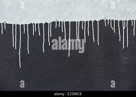 Grauer Farbe fällt auf eine dunkle graue Wand Stockfoto