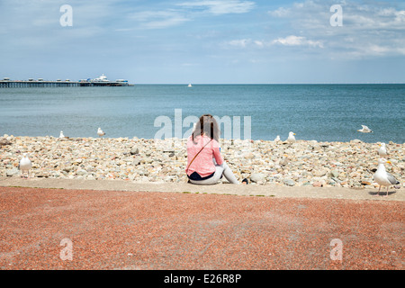 Junge Frauen sitzen auf ihrem eigenen am Strand trinken Kaffee, umgeben von Möwen als sie genießt den Blick aufs Meer Stockfoto