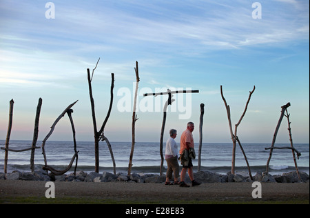 Ein paar gehen vorbei an Treibholz Zeichen für Hokitika auf der Strandpromenade, West Coast, Südinsel, Neuseeland Stockfoto