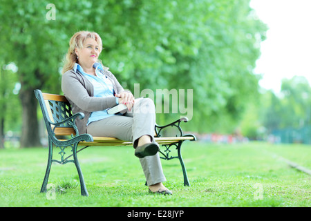 Reife Dame entspannend in einem Park auf einer Bank sitzend Stockfoto