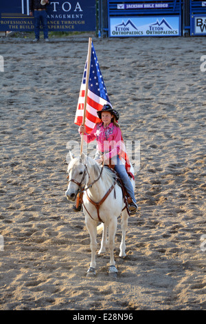 11 Jahre altes Mädchen auf einem Pferd trägt die Flagge bei der Eröffnung des Jackson Hole Rodeo. Stockfoto