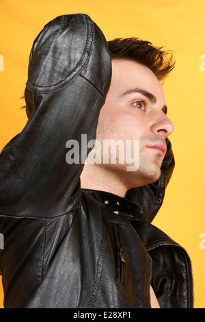 Ernst junger Mann mit schwarzer Lederjacke, Blick in die Kamera über einen gelben Hintergrund. Stockfoto