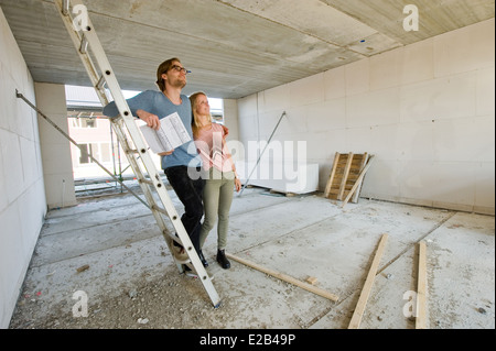 Junges Paar mit Blaupause sucht glücklich wie ihr neue Zuhause entsteht. Stockfoto