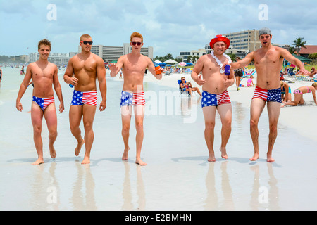 Eine Gruppe von patriotischen College-Alter Männer in Badeanzügen Sternenbanner strut ihre Sachen am Strand am 4. Juli Stockfoto