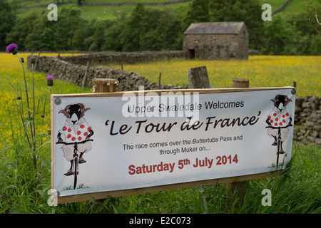 Banner auf der Route der Tour de France (Yorkshire) begrüßen die Besucher Swaledale, traditionelle Scheune & gelb blühende Wiese jenseits - England, UK. Stockfoto