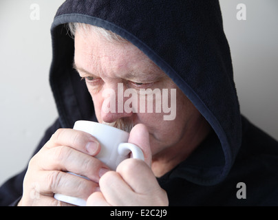 Senior in schwarzer Jacke mit Händen um eine Kaffeetasse Stockfoto