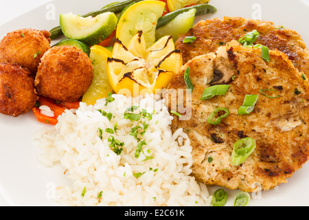 Pfanne gebraten Krabbe Kuchen Sandwich serviert mit einer Seitenlänge von Reis, Gemüse Medley und Hush Welpen. Stockfoto