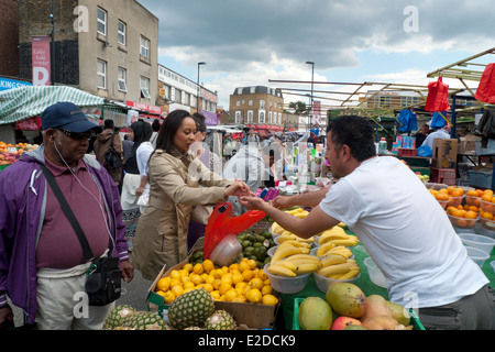 Eine Kundin, die einen Händler an einem Obststand auf dem Ridley Road Market in der Kingsland Road Dalston East End London E8 UK BEZAHLT, KATHY DEWITT Stockfoto