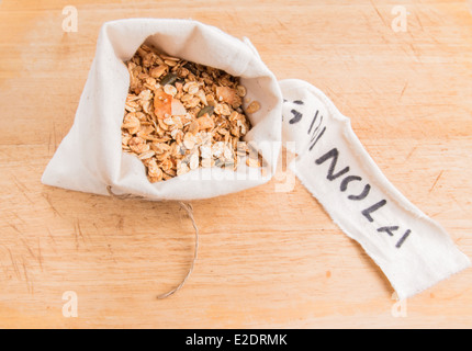 Müsli in einem cremefarbenen Stoffbeutel mit einem Etikett auf einem Holzbrett (11 von 15) Stockfoto