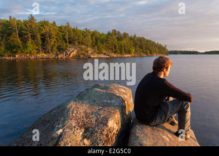 Ein Mann sitzt auf einem Felsen bei Sonnenuntergang über die Georgian Bay. Massasauga Provincial Park, Ontario, Kanada. Stockfoto