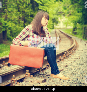 junger Teenager trauriges Mädchen mit Koffer sitzen auf den Schienen Stockfoto