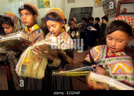 Pakistan Khyber Pakhtunkhwa Kalash Täler Bumburet Tal Schule Brun Dorf junge Schulmädchen Kalash stehend mit großen offenen Bücher in ihren Händen, ihren Unterricht zu wiederholen Stockfoto