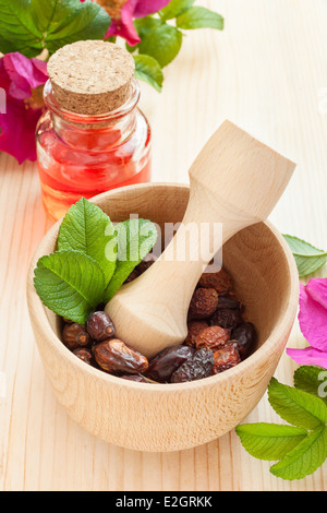 ätherisches Öl in Glasflasche, getrockneten Hagebutten Beeren in Mörtel und Hagebutten Holzblumen auf Tisch Stockfoto