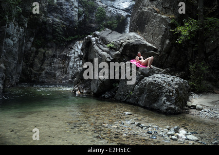 Eine Frau, die auf einem Felsen nahe einem Wasserfall auf dem Fonias Fluß liegt, auf der nordgriechischen Insel Samothraki, Nord-Ägäis, Thrakien, Griechenland. Stockfoto