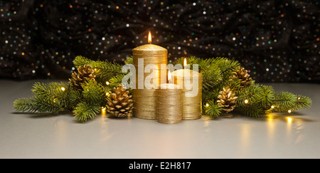 Drei goldene Kerzen mit Weihnachtsbaum Äste und Tannenzapfen dekoriert Stockfoto
